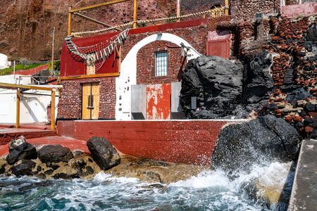 splash of water from aegean sea near red building on greek islandの写真素材