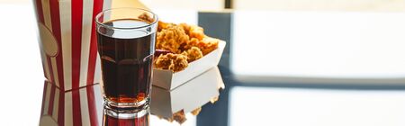 deep fried chicken, striped bucket and soda in glass on glass table in sunlight near window, panoramic orientationの写真素材