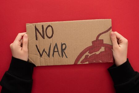 cropped view of woman holding cardboard placard with no war lettering and bomb on red backgroundの写真素材