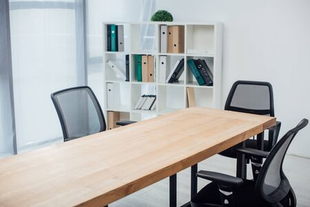Wooden table and chairs near rack with paper folders in officeの写真素材