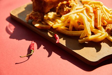 selective focus of spicy deep fried chicken and french fries served on wooden cutting board in sunlightの写真素材