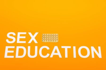 top view of sex education lettering near blister pack with contraceptive pills isolated on orangeの写真素材
