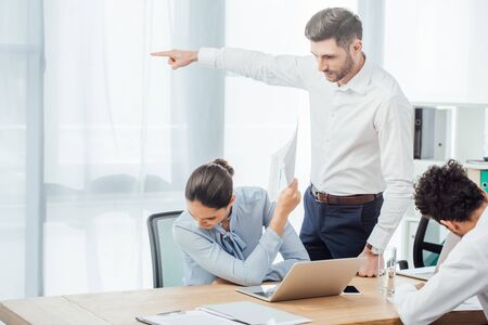 Businessman pointing with finger near mexican businesswoman holding document in officeの写真素材