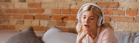 Panoramic shot of dreamy kid in headphones sitting on couchの写真素材