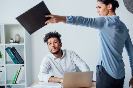 Selective focus of mexican businesswoman holding clipboard near african american businessman at table in officeの写真素材