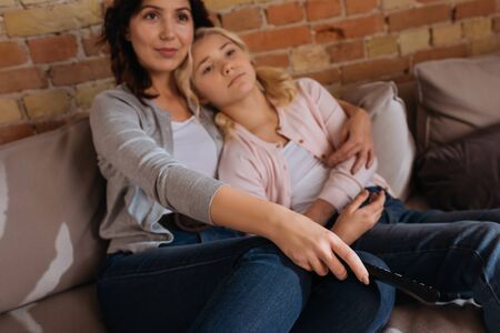 Selective focus of woman holding remote controller and hugging child on couchの写真素材