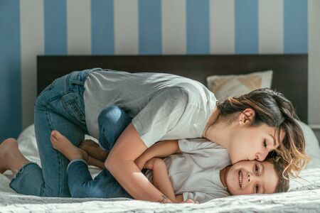 mother kissing cheek of cute toddler son on bedの写真素材