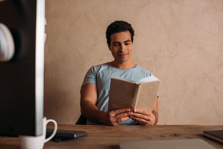 happy mixed race freelancer reading book in home office during quarantine