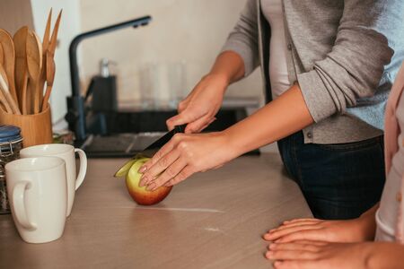 Cropped view of mother and daughter cutting fresh apple on kitchen worktopの写真素材