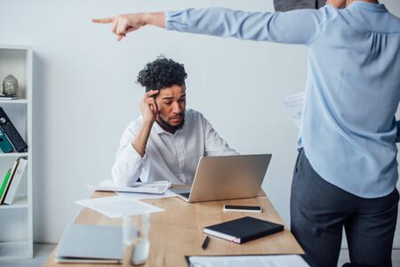 Selective focus of african american man using laptop near businesswoman pointing with finger in officeの写真素材