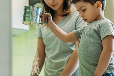 selective focus of toddler boy holding baking sieve with flour near motherの写真素材