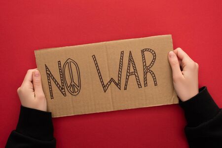cropped view of woman holding cardboard placard with no war lettering on red backgroundの写真素材