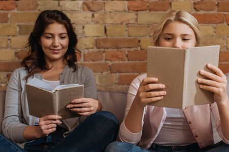 Selective focus of smiling woman with child reading books on couch