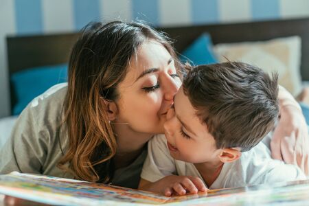 attractive mother kissing cheek of cute toddler boy at homeの写真素材