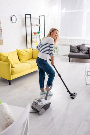 Attractive woman smiling and cleaning up with vacuum cleaner in living roomの写真素材