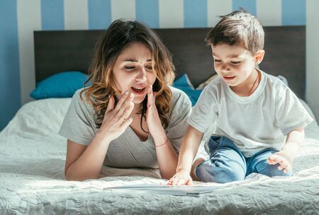 shocked woman looking at laptop near toddler son in bedroomの写真素材