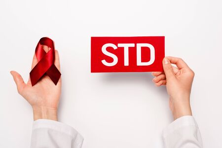 cropped view of doctor holding paper with std lettering and red ribbon on whiteの写真素材