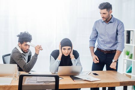 Muslim businesswoman covering ears near multiethnic colleagues in officeの写真素材