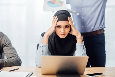 Sad arabian businesswoman looking at camera near colleagues in officeの写真素材