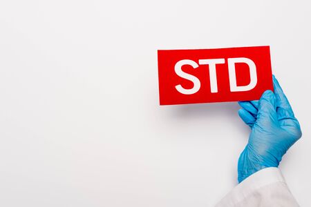cropped view of doctor in blue latex glove holding paper with std lettering on whiteの写真素材