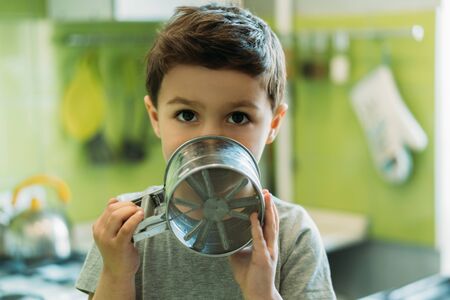 cute toddler boy covering face with baking sieve at homeの写真素材