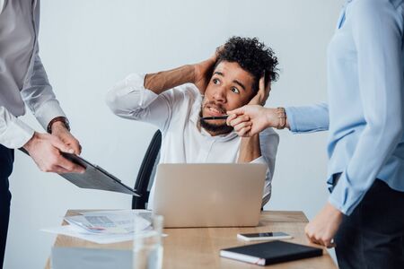Selective focus of business people standing near scared african american businessman in officeの写真素材
