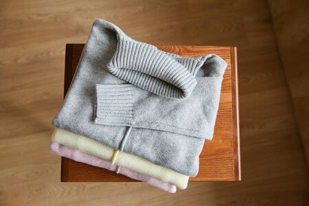 top view of pink, beige and grey knitted soft sweaters on wooden table in room