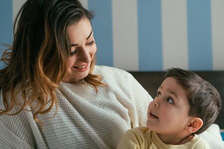 happy mother and adorable son looking at each other in bedroom