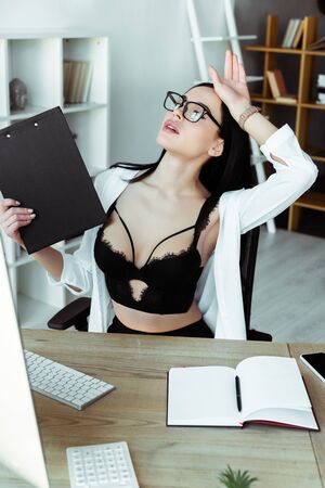 Selective focus of sensual secretary in bra holding clipboard at working tableの写真素材