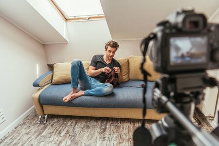 selective focus of young video blogger knitting on sofa while looking at digital cameraの写真素材