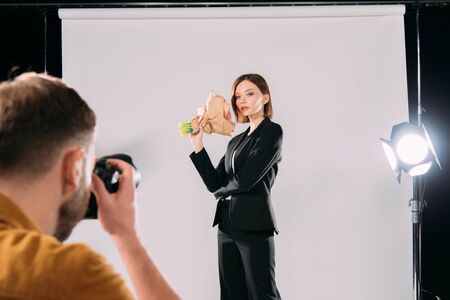 Selective focus of photographer taking photo of elegant model with bouquet in photo studioの写真素材