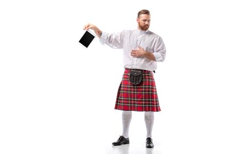displeased Scottish redhead man in red kilt with digital tablet on white backgroundの写真素材