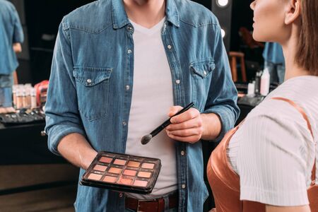 Cropped view of makeup artist holding set of blush and cosmetic brush near model in photo studioの写真素材