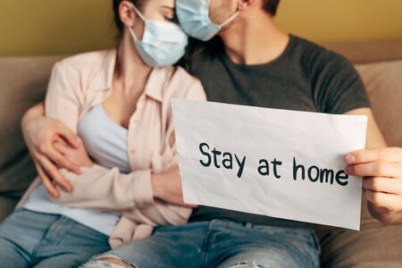 selective focus of man hugging girl in medical mask and holding placard with stay home letteringの写真素材