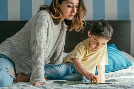 beautiful woman looking at son playing board game on bedの写真素材