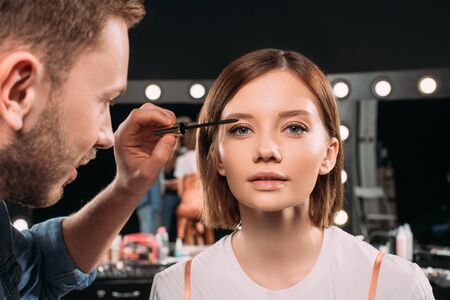 Selective focus of makeup artist applying mascara on young model in photo studio