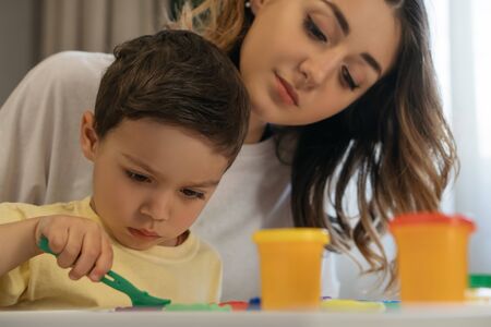 young mother looking at concentrated son holding spatula near plasticine