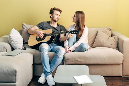 handsome man playing acoustic guitar near attractive girl and digital tablet with white screenの写真素材