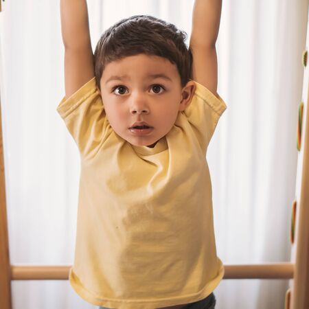 adorable child hanging on horizontal bar while exersicing in home gym