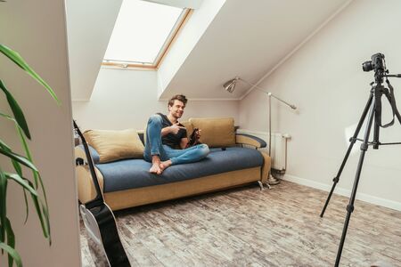 handsome vlogger pointing with finger while knitting on sofa at home in attic room