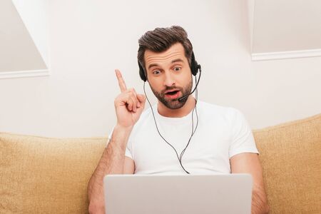 Surprised teleworker in headset pointing with finger during video chat on laptop at home