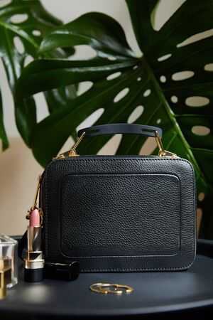leather handbag near golden earrings and lipstick on black table near tropical leavesの写真素材