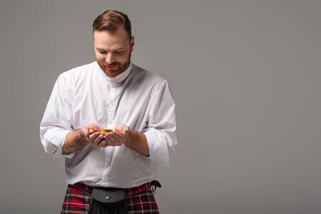 Scottish redhead man in red kilt with gold coins on grey backgroundの写真素材