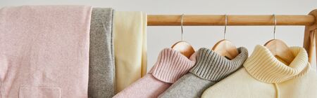 close up view of pink, beige and grey knitted soft sweaters and pants hanging on wooden rack...