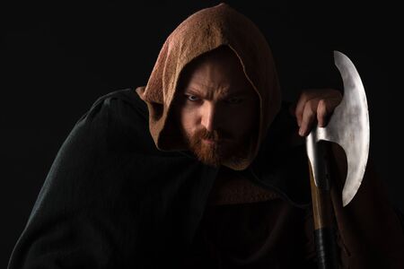 portrait of frowning medieval Scottish warrior with battle axe in mantel isolated on black