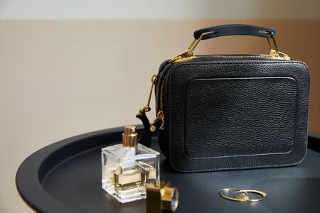 leather handbag near golden earrings, perfume on black table on beige backgroundの写真素材