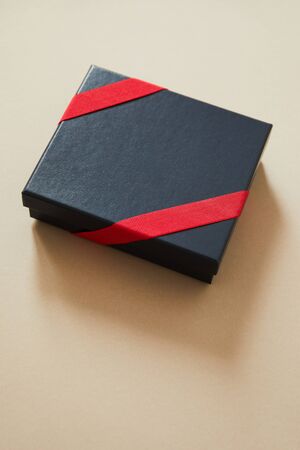 black gift box with red ribbon on beige background