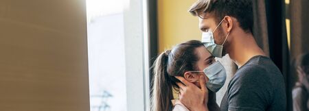 panoramic crop of man in medical mask kissing forehead of woman at home