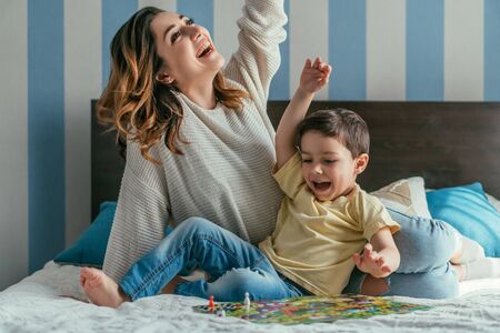 excited mother and son showing winner gestures while playing board game on bedの写真素材