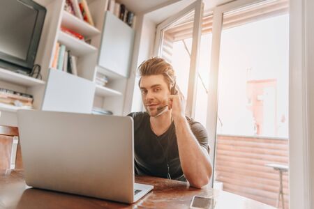 smiling man looking at camera while working at home near laptopの写真素材